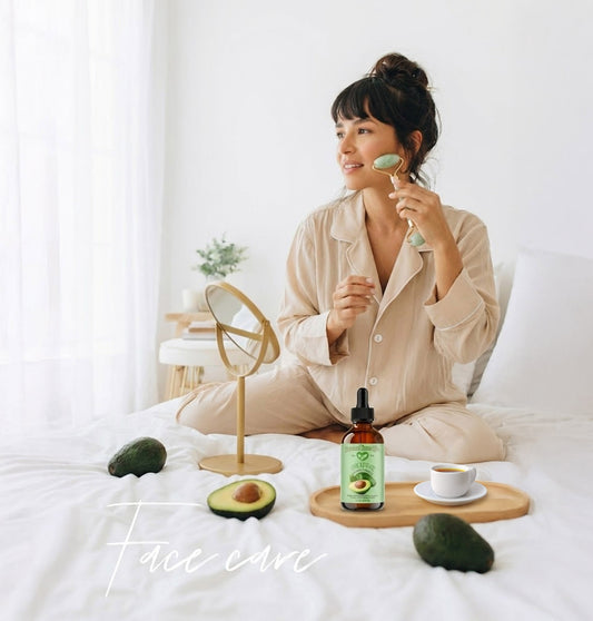 Woman in pajamas applying facial oil with a brush on a white bed, surrounded by avocados and a bottle of oil.